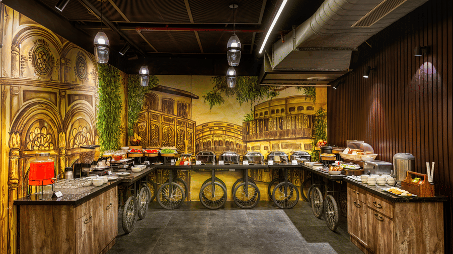View of the restaurant buffet counter at Lords Inn Amritsar with ornate wall murals, overhead lighting, and a spread of food stations.