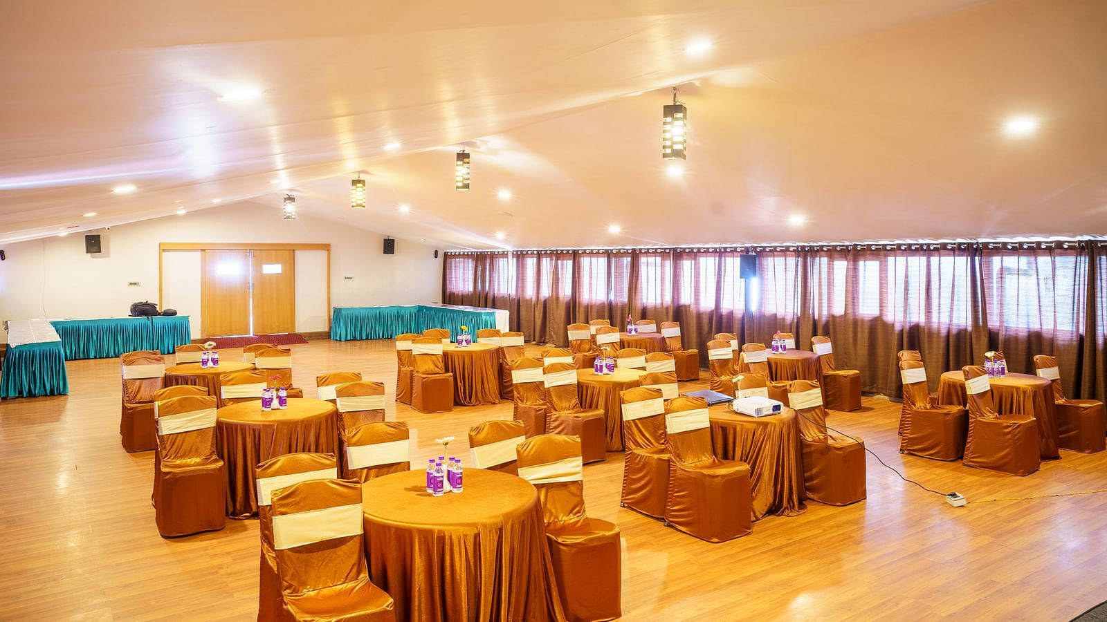 A spacious event hall at Orsino Hotel & Spa arranged with round tables draped in gold and matching chair covers, ready for a gathering.