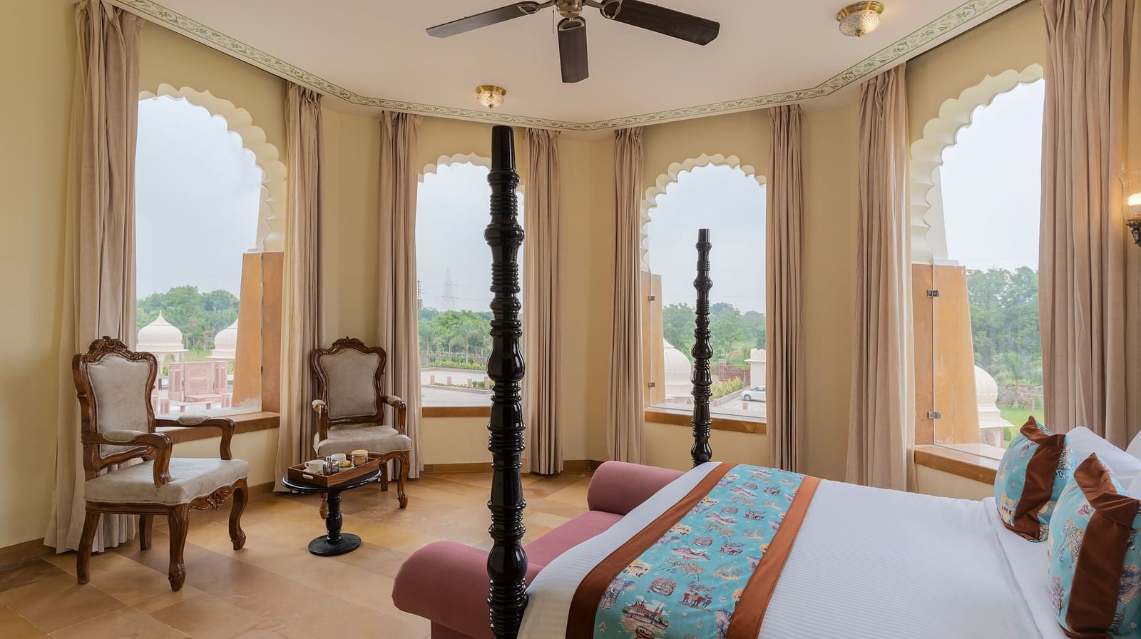 Elegant bedroom with arched windows overlooking scenic landscape at Kesar Bagh Palace.