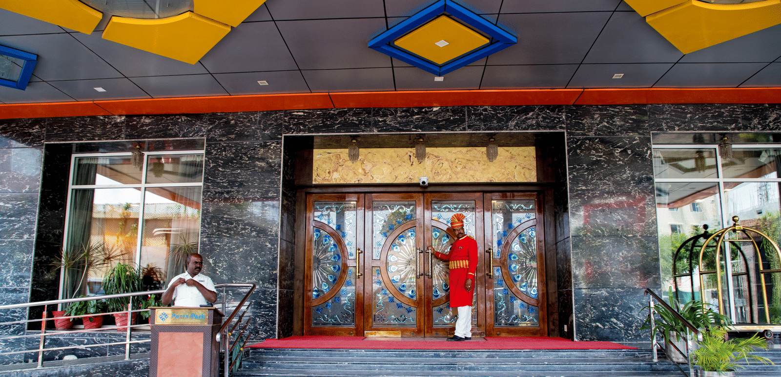 Entrance of Benzz Park, Vellore, featuring a doorman wearing a red coat ready to open the door for the guest.