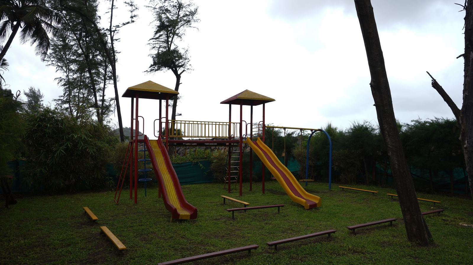 A children's playground with slides and swings on a grassy area surrounded by trees - Tranquil Beach Resort, Harihareshwar