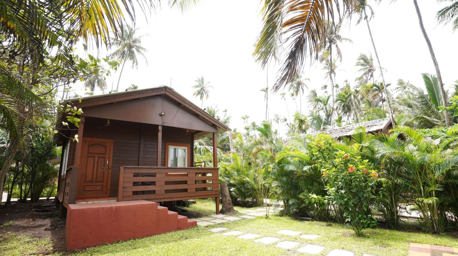 A wooden cottage nestled amidst lush green surroundings - Tranquil Beach Resort, Harihareshwar