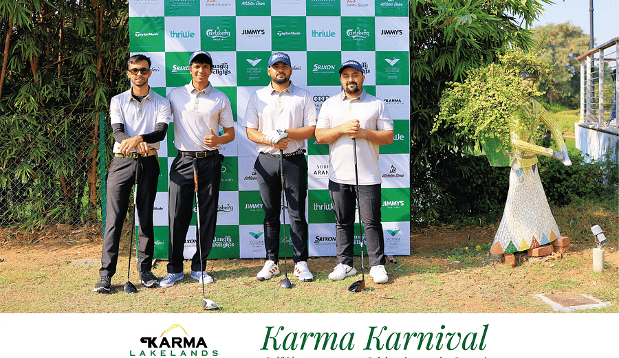 Four men in casual and golf attire smiling and holding their clubs while posing at the Karma Karnival event backdrop.