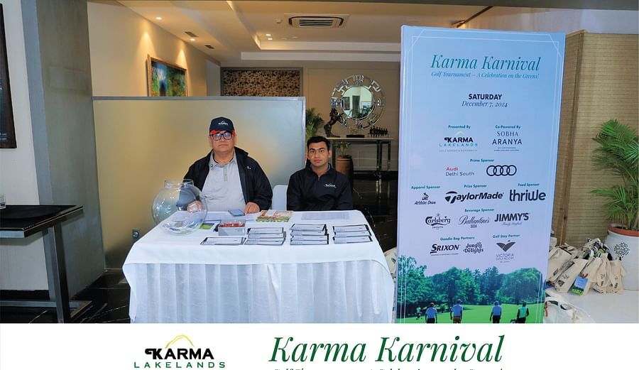 Two individuals seated at an indoor registration desk with Karma Karnival banners in the background.