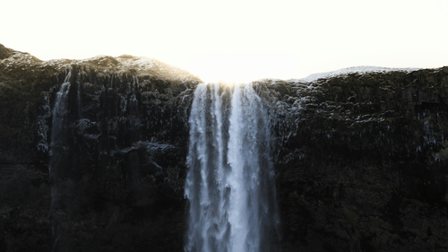 Waterfall cascading down a cliff with sunlight shining through.