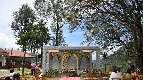 An outdoor wedding space at Ibex Resorts, Coonoor (Leewood), featuring wedding arrangements, and people seated with the trees in the backdrop.