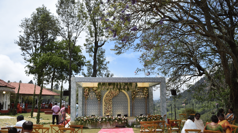 An outdoor wedding space at Ibex Resorts, Coonoor (Leewood), featuring wedding arrangements, and people seated with the trees in the backdrop.