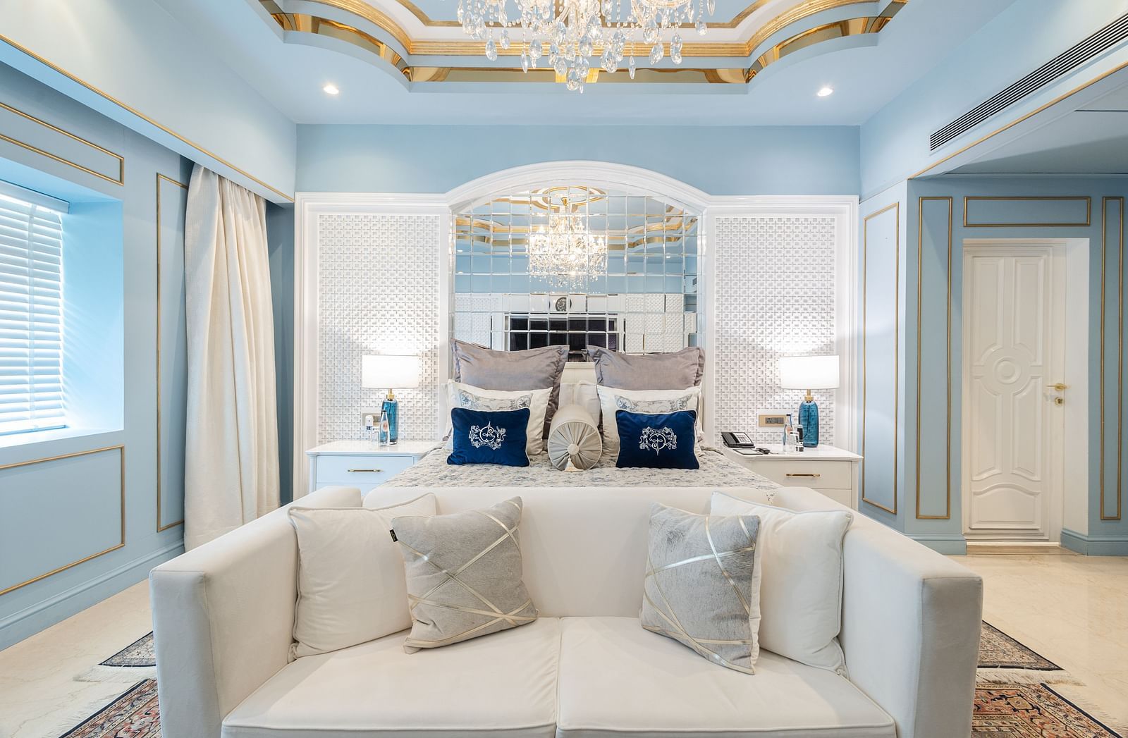 Claridges Suite at The Claridges New Delhi, highlighting the front view of a plush bed flanked by bedside lamps and illuminated by a chandelier overhead
