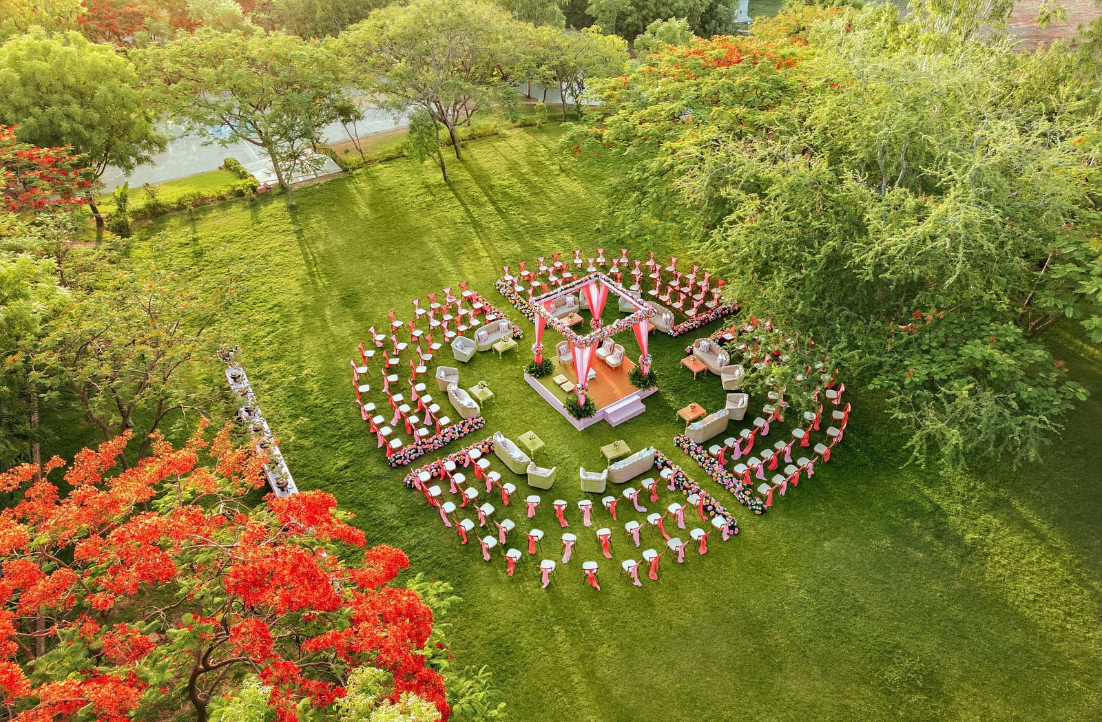 Aerial view of an elegant setting of chairs facing towards the stage in a lawn on a sunny day at Essentia Luxury Resort & Spa, Udaipur. 
