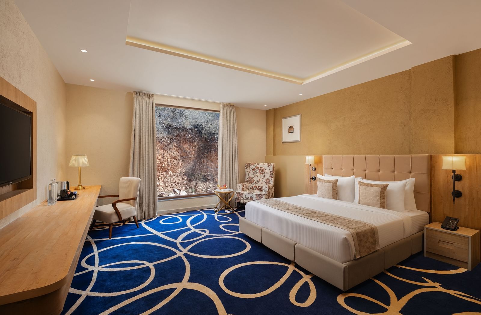 Deluxe room with a king size bed placed in front of a TV at Essentia Luxury Resort & Spa, Udaipur.