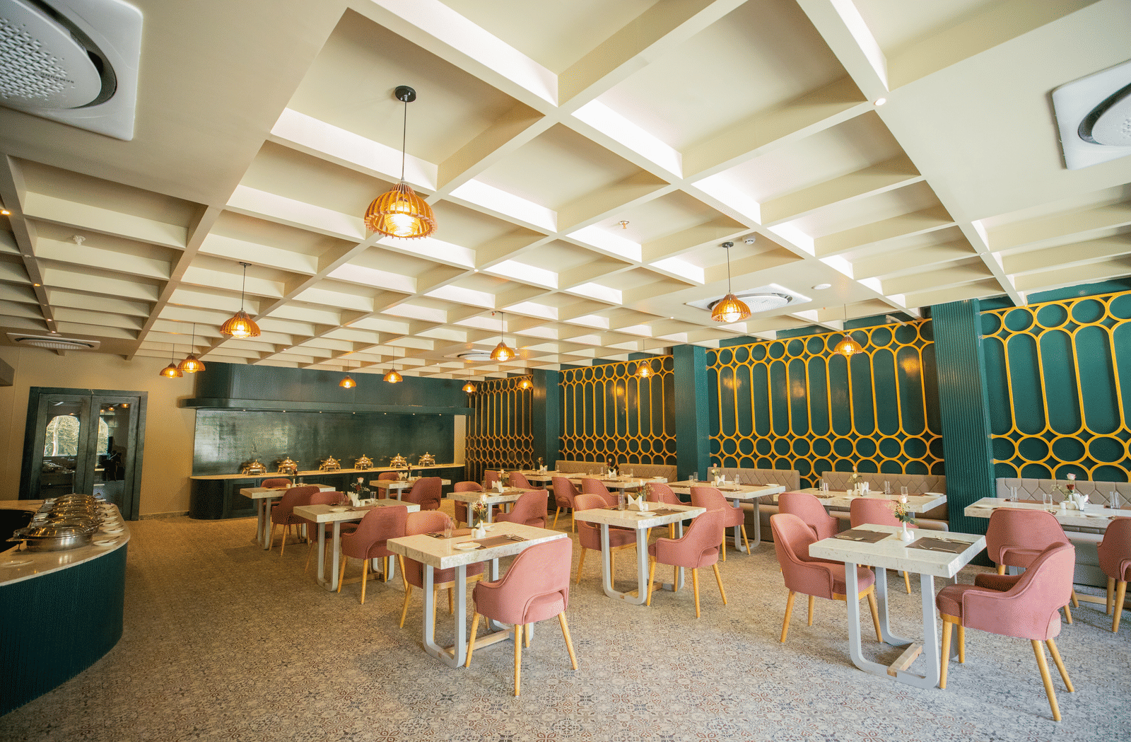 A dining setting of Blue Salt and Coffee at Essentia Luxury Resort & Spa, Udaipur featuring 2-seater and 6-seater tables under patterned ceiling