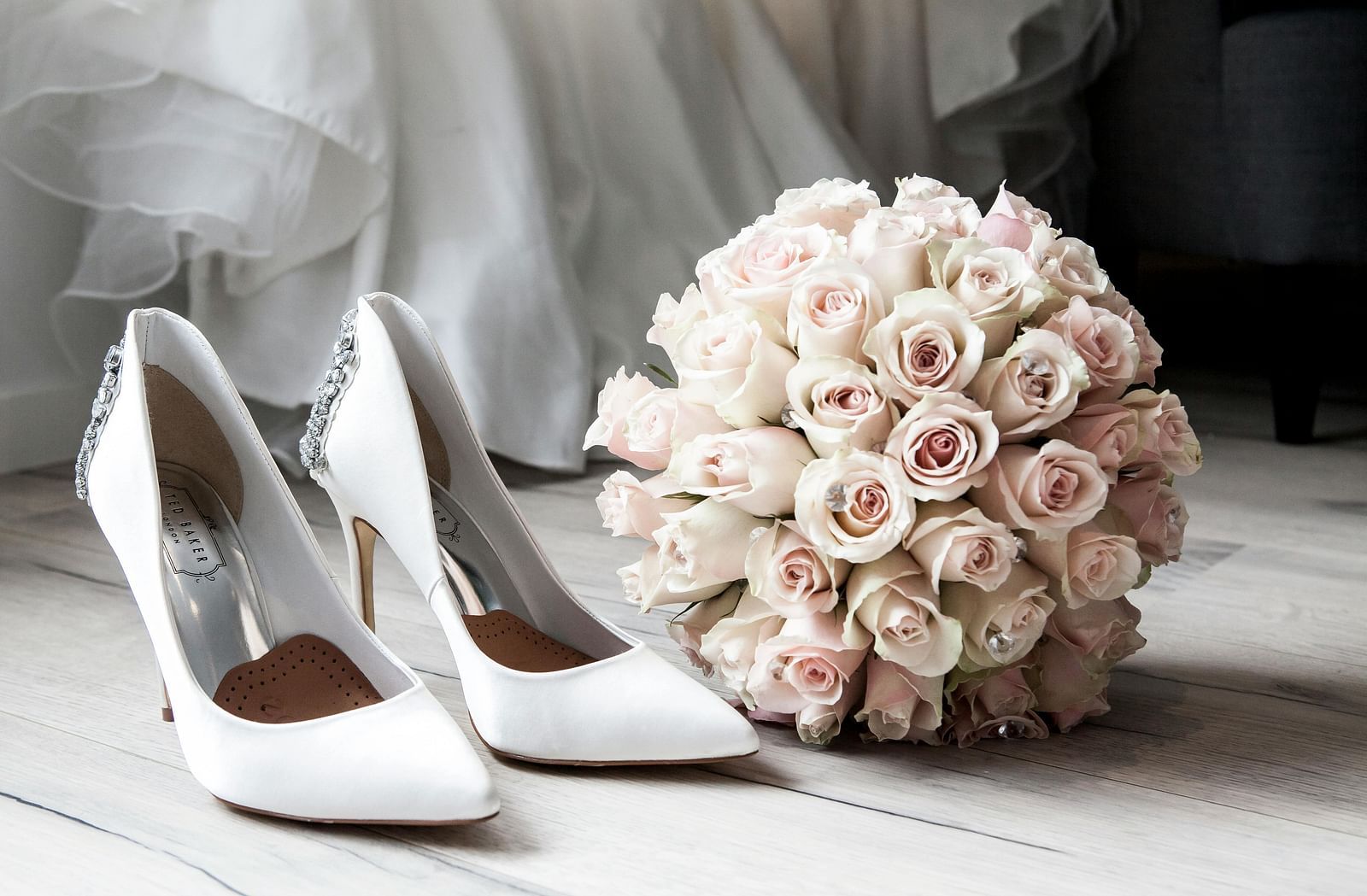A white pair of heels placed next to a flower bouquet.