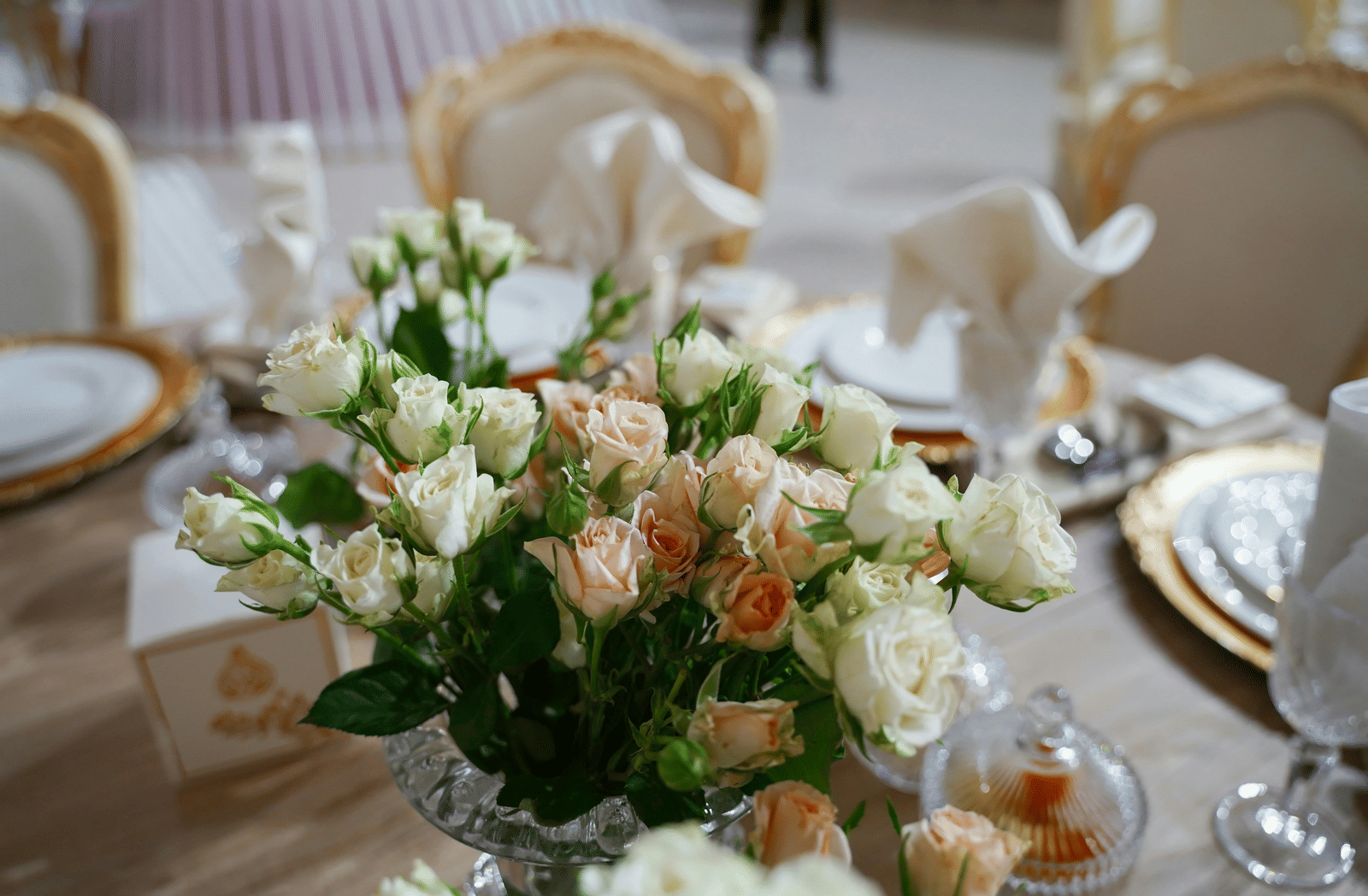 A close up shot of a beautiful flower vase with a lot of white and pink roses on a dining table.
