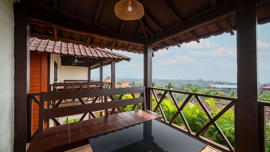 An image showing a balcony view with greenery, shot from a room with wooden details and benches