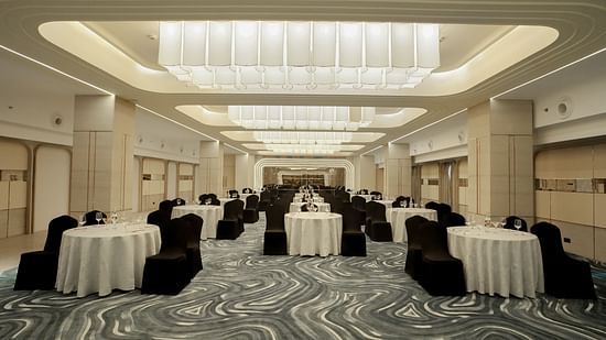 Spacious event venue with round tables covered in white cloths and black chairs. Bright overhead lighting and patterned floor - The Orchid Hotel, Chandigarh
