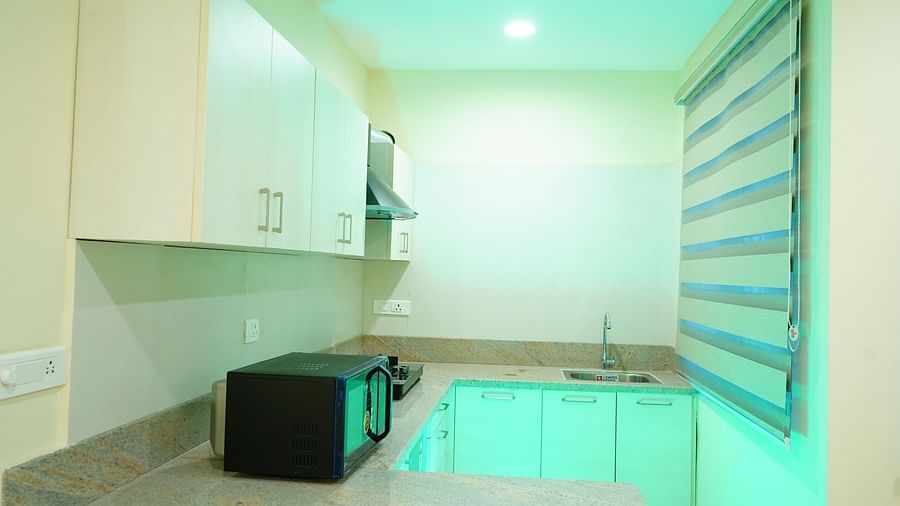 A kitchen area featuring a microwave, a sink, storage cabinets, a cooking stove and a chimney - A M Suites