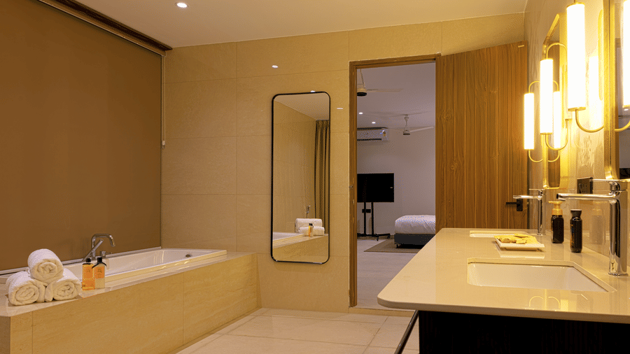  Bathroom at SUKAVI with a built-in bathtub on the left, a vanity with 2 sinks on the right, and a full-length mirror between the bathtub area and doorway.