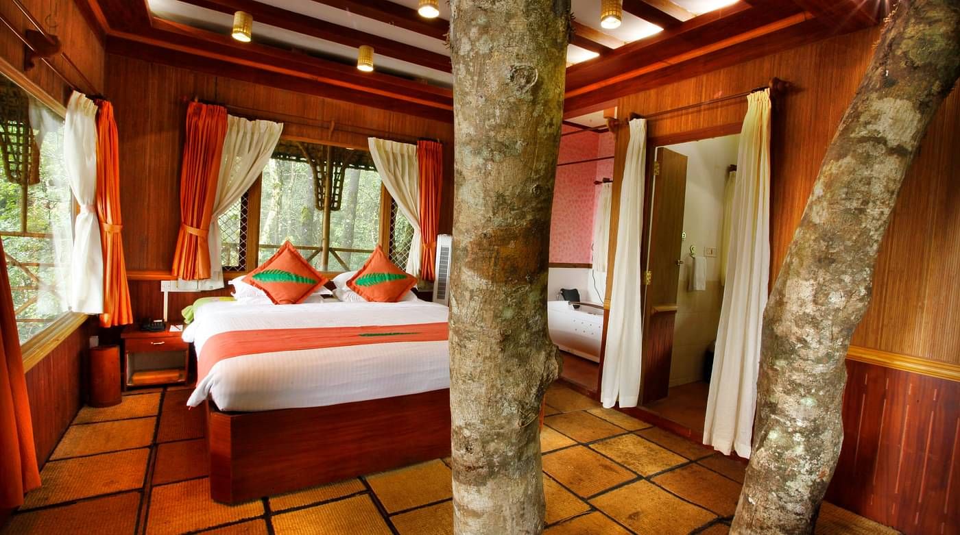 Room with a bed and tree trunks protruding out of the floor at Vythiri Resort, Wayanad
