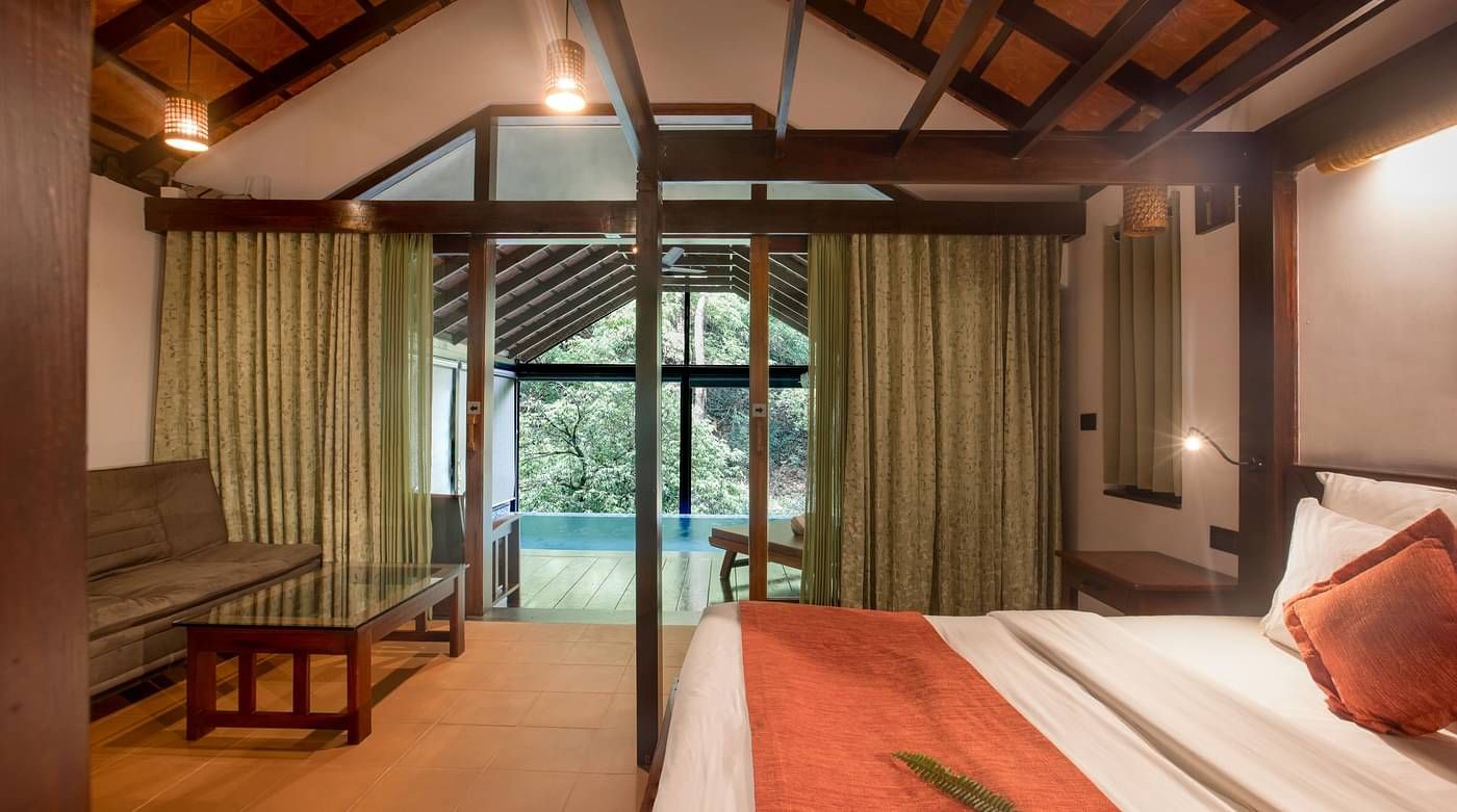 A side view of a bed in a room that has forest views | Vythiri Resort. Wayanad