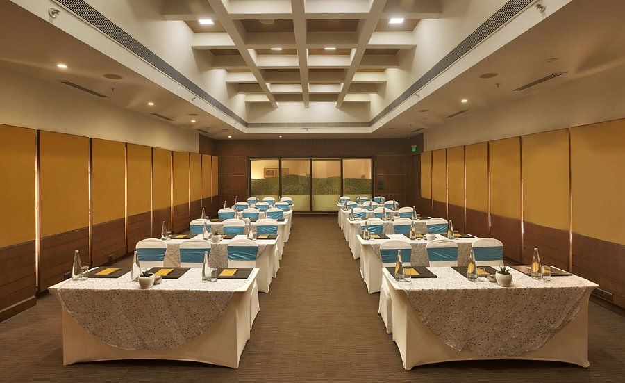 Modern conference room with rows of tables, blue and white chair covers, and a structured ceiling - Heritage Village Resorts & Spa.