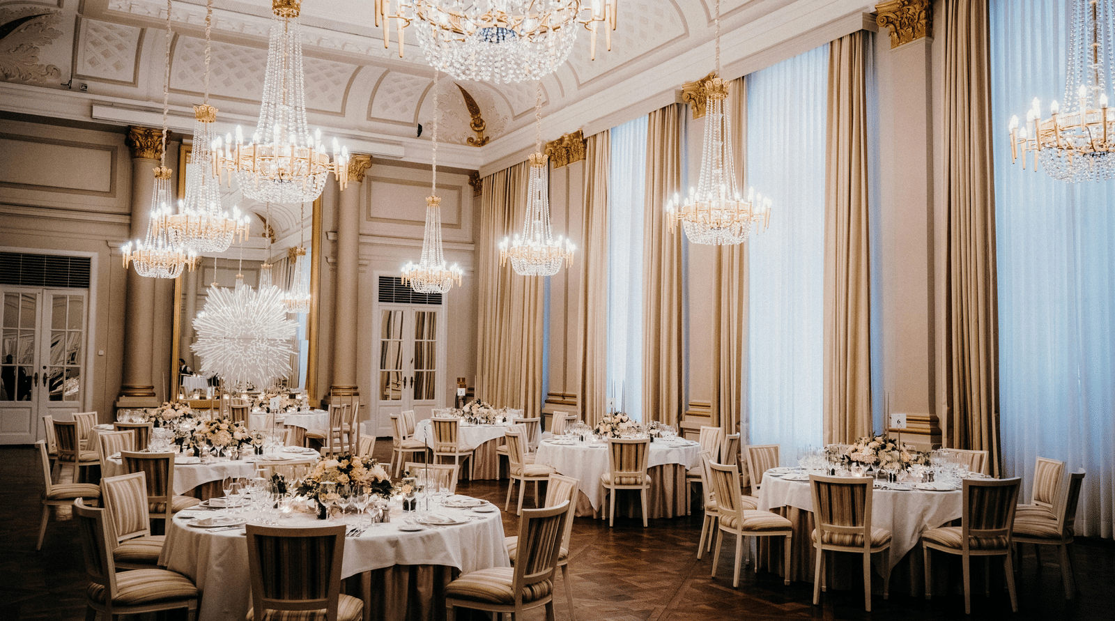 A view of a lavish ballroom, tables adorned with linens and elegant decor.