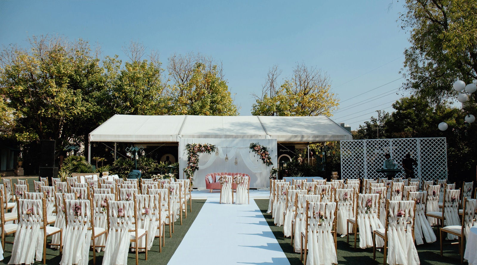 A wedding aisle with chairs and a stage under a canopy in an open lawn.