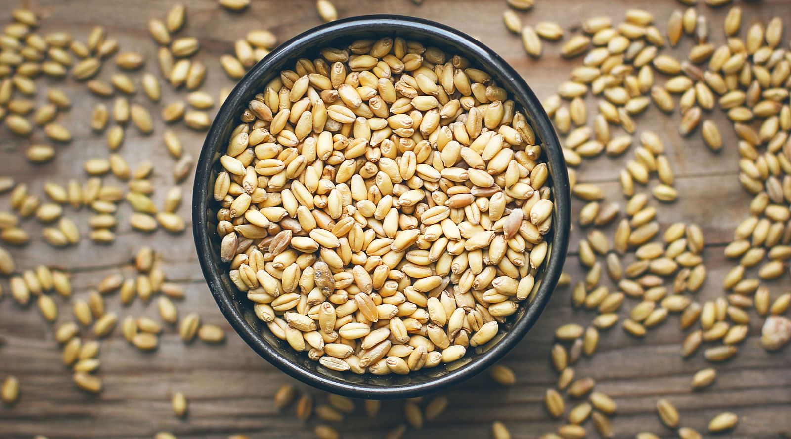 A top view of black bowl filled with wheat on a wooden surface.