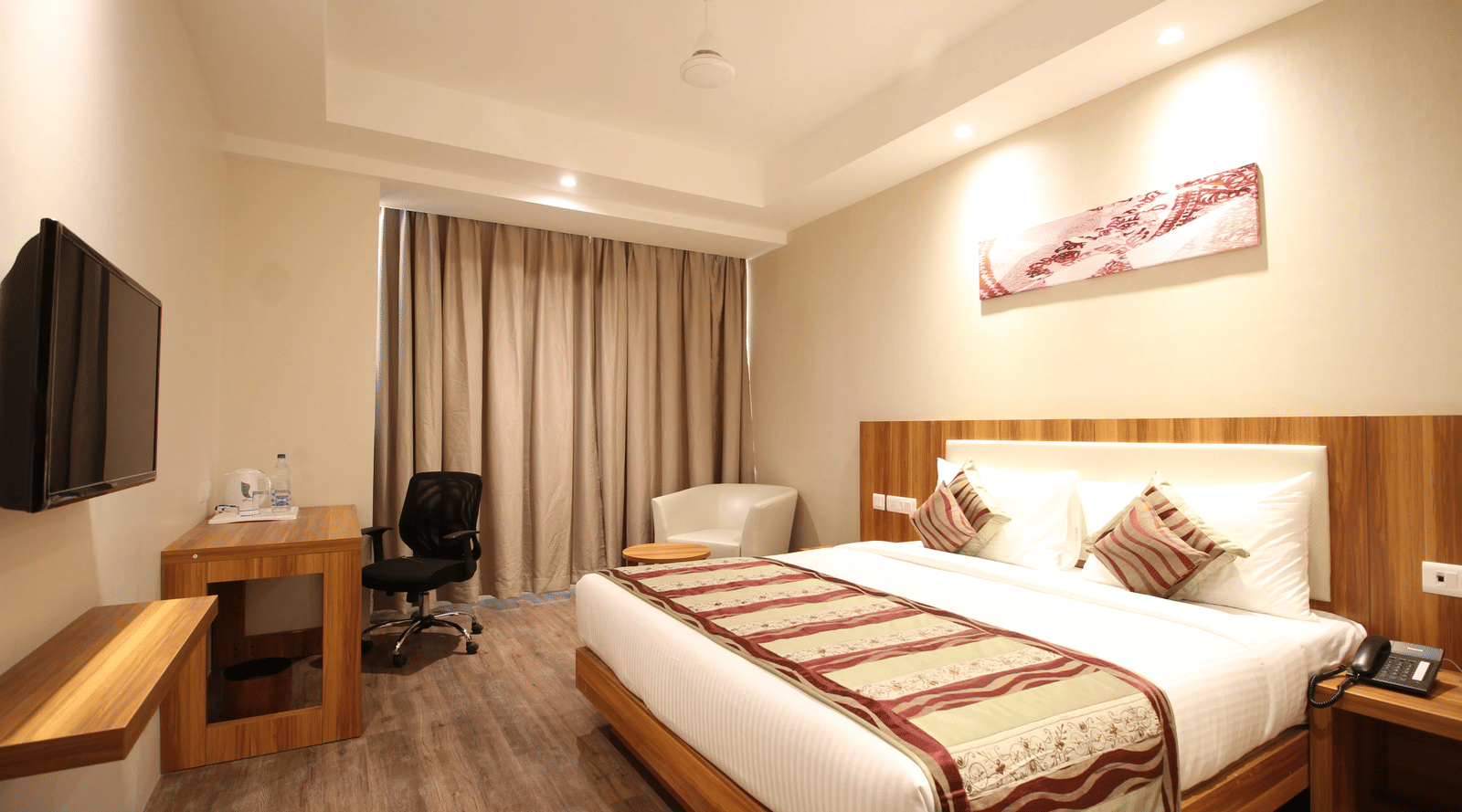 A double bed in a well-lit bedroom with a wall-mounted television at Le ROI Corbett Resort.