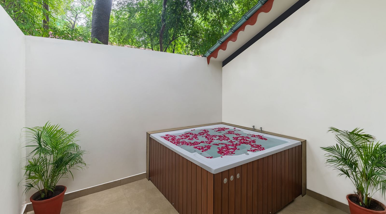 image featuring an outdoor Jacuzzi with two pots with lush green bushes along with rose petals spread across the water at the luxury family suite in aranya vilas 