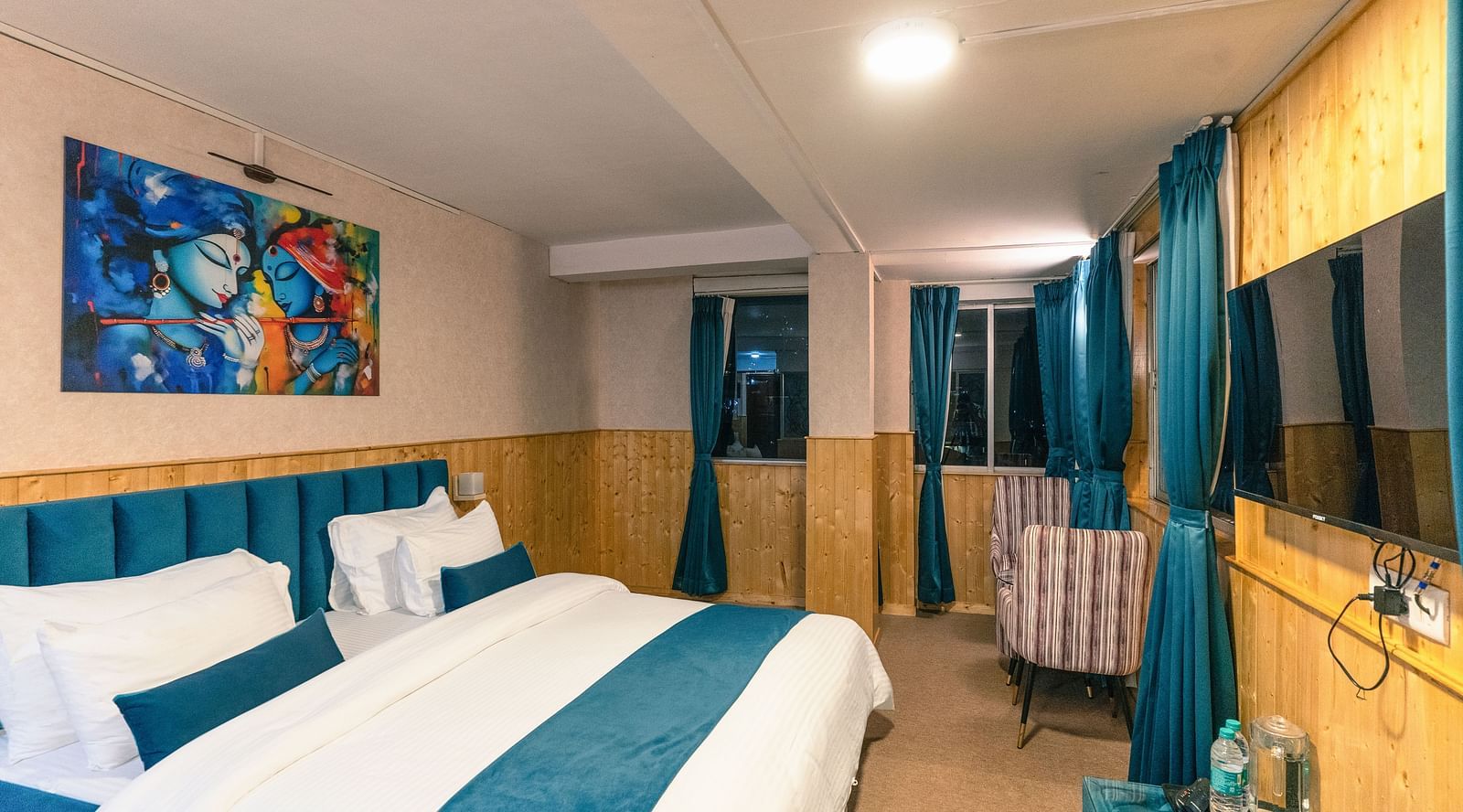 Deluxe Room with a king size bed, inviting ambiance, wooden bedside table, and a wall mounted television at Avianna Seven Seas, Darjeeling.