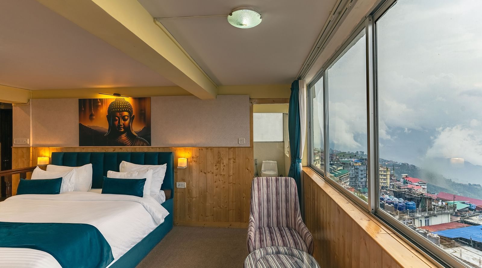 Suite with a king size bed, wall-mounted television, wooden table, and cosy lighting along with large window with city viewat Avianna Seven Seas, Darjeeling