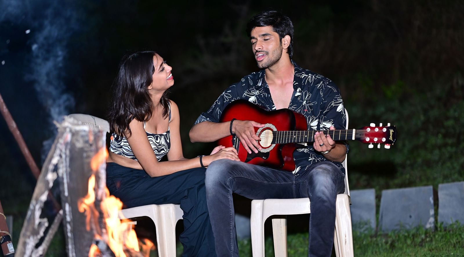 Couple playing guitar by a campfire at a camping site | Diamond Parks, Pune