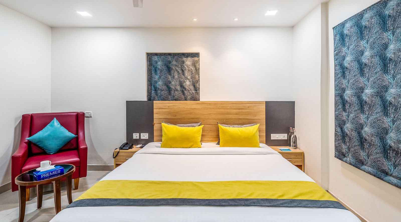 Shot of a bed in a room at the hotel, a red single couch and a small tea table | Eminent Suites & Apartments, Hi-Tech City