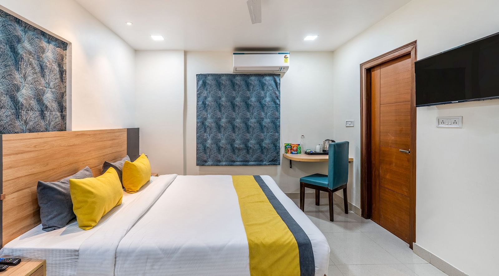 A side-angle view of the room at the hotel featuring a king size bed, air conditioner, flat screen television, side table and a chair | Eminent Suites & Apartments, Hi-Tech City