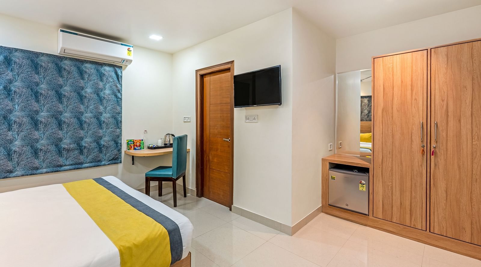  A wide angle shot of a bed in a room at the hotel featuring a flat screen television, a study table, chair, wooden cupboard | Eminent Suites & Apartments, Hi-Tech City