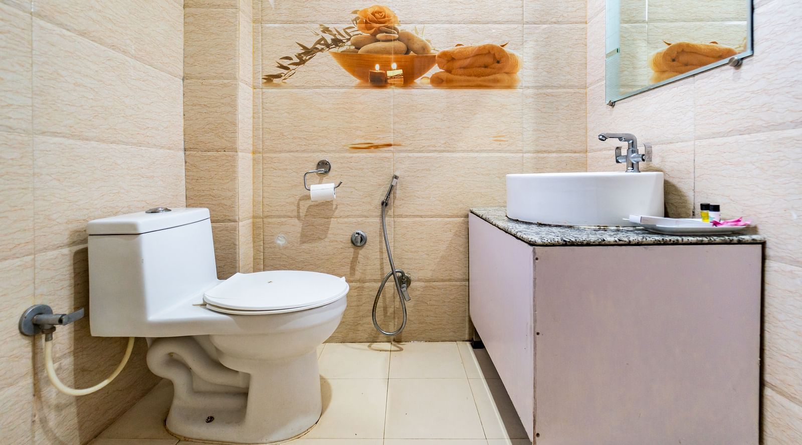 A bathroom with a Commode, sink, mirror and tiled walls at Flutter Hotels and Resorts.