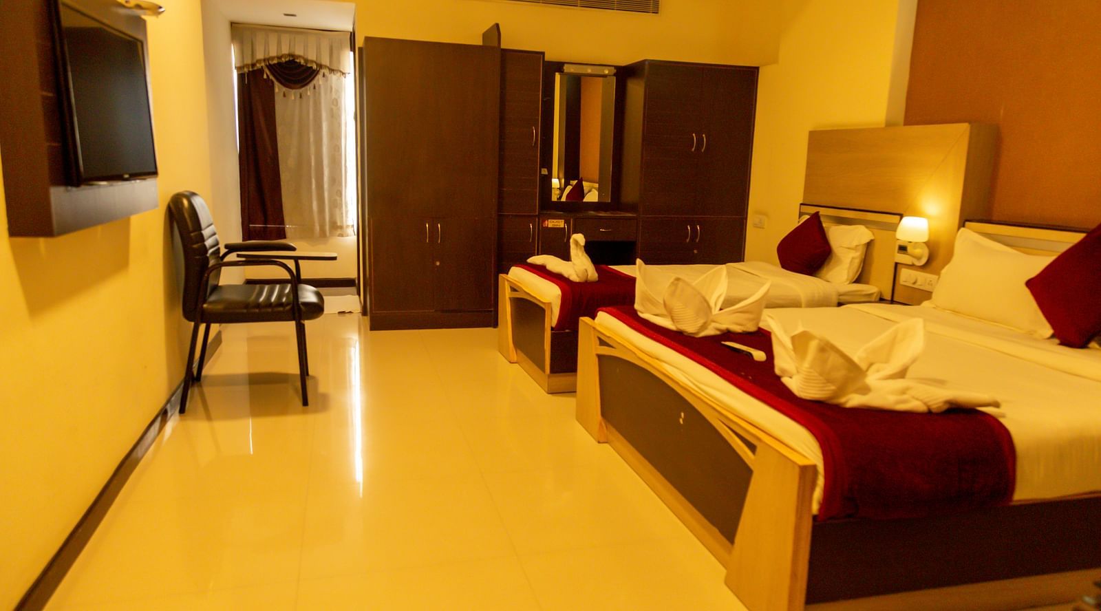 a bedroom with a large bed and a single bed facing a mounted television - Hotel Rockfort View, Trichy