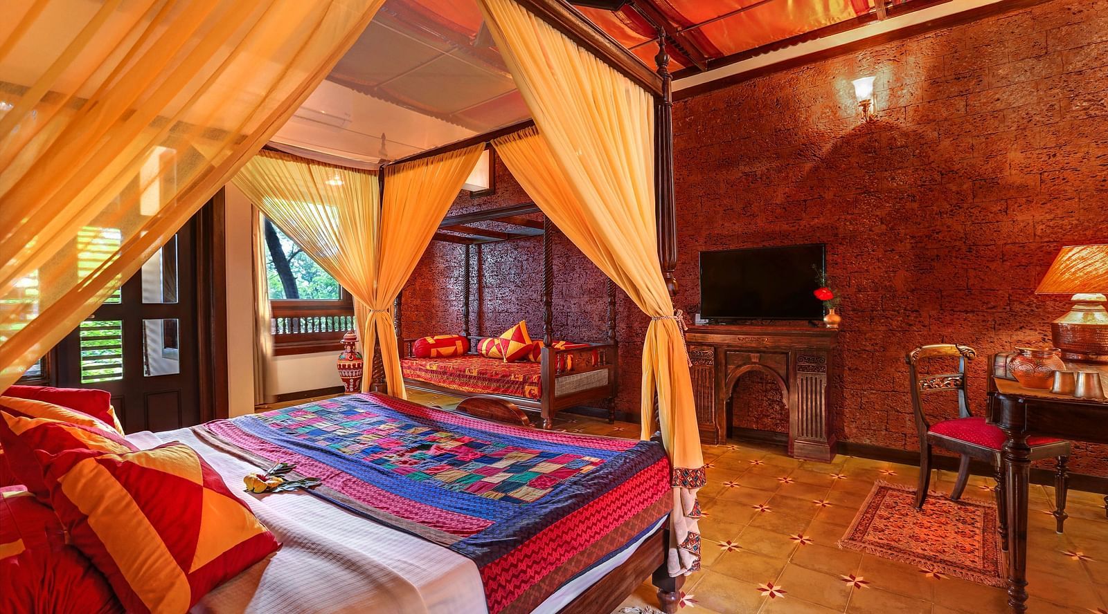 An image of a master suite bedroom with poster bed, windows, flat TV screen, wooden table, lamp, and many more - Hoysala Village Resort, Hassan