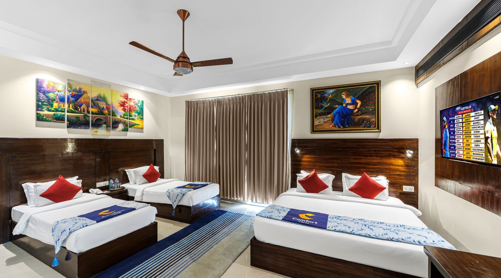 Well furnished huge room with a king size bed and twin beds featuring a ceiling fan, artwork above bedside table, and TV unit opposite the beds at Inder Reva Resorts Rishhikesh.