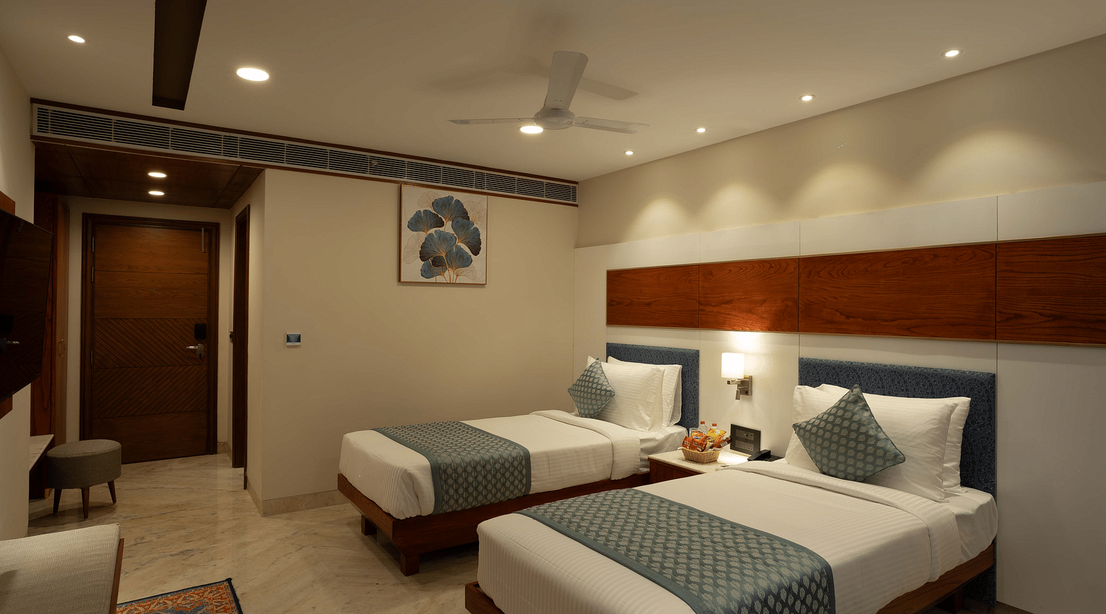 Deluxe Room with twin beds along with a wooden side table with a lamp and wooden table and chair at Inde Signature Jaipur