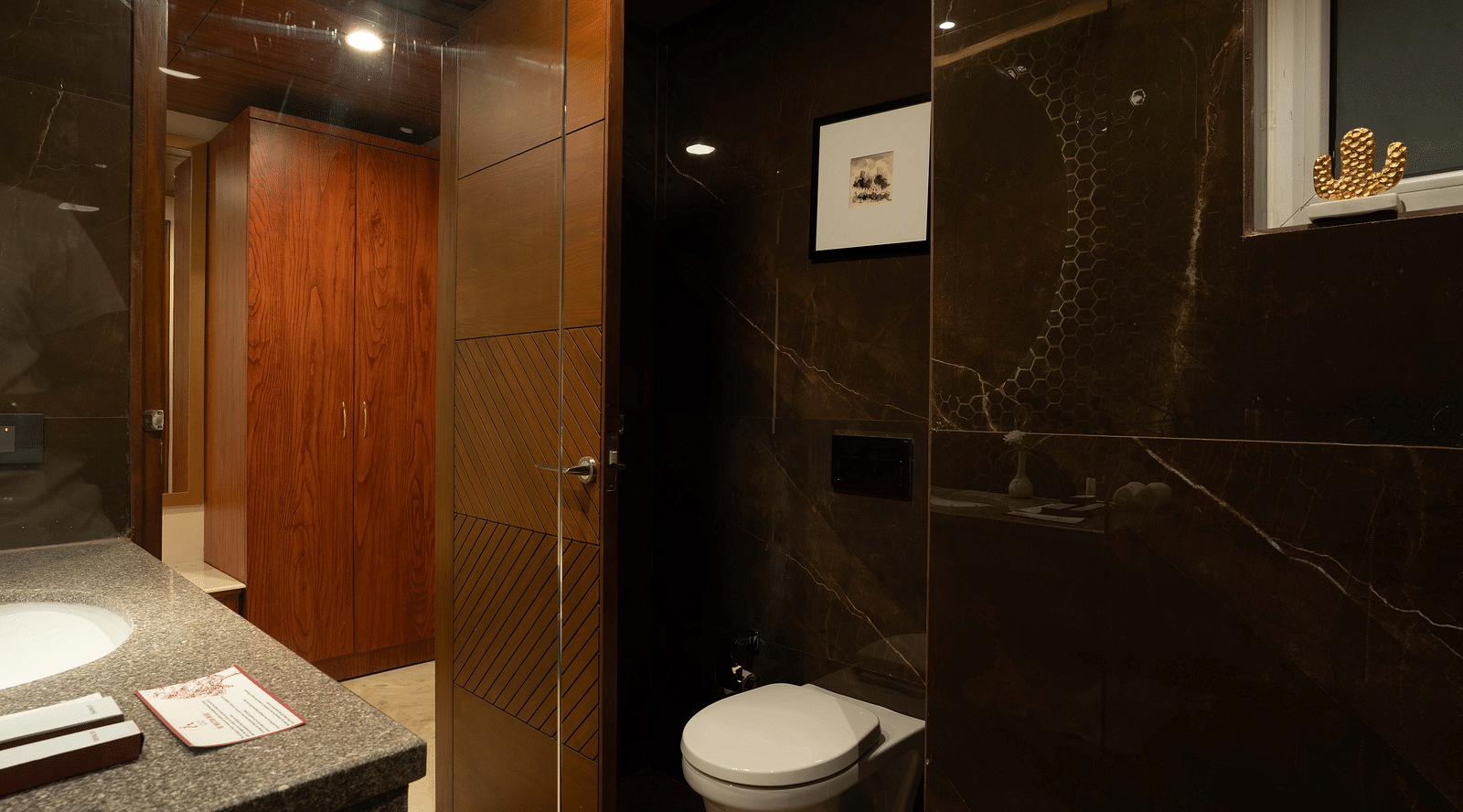 Transparent glass divider separating the showering and toilet areas in the Deluxe room's bathroom at Inde Signature Jaipur.
