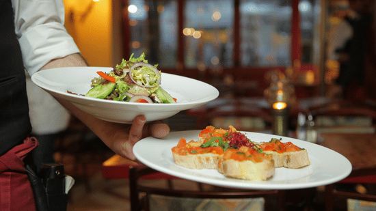 a person in a restaurant holding two plates with delicious cuisines in it that are well plated