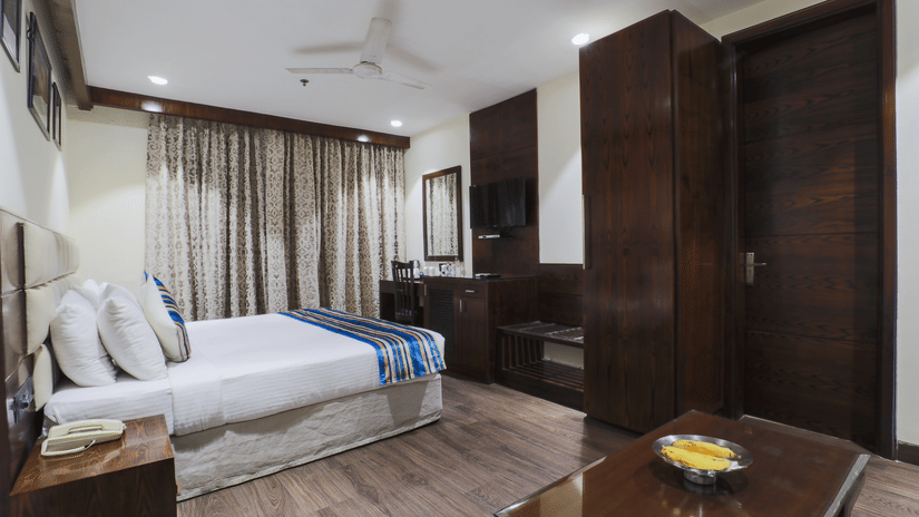 Spacious room with modern interiors, cozy bedding, and elegant wooden furnishings at Hotel Bluestone (Nehru Place) by The Cosy Hotels.