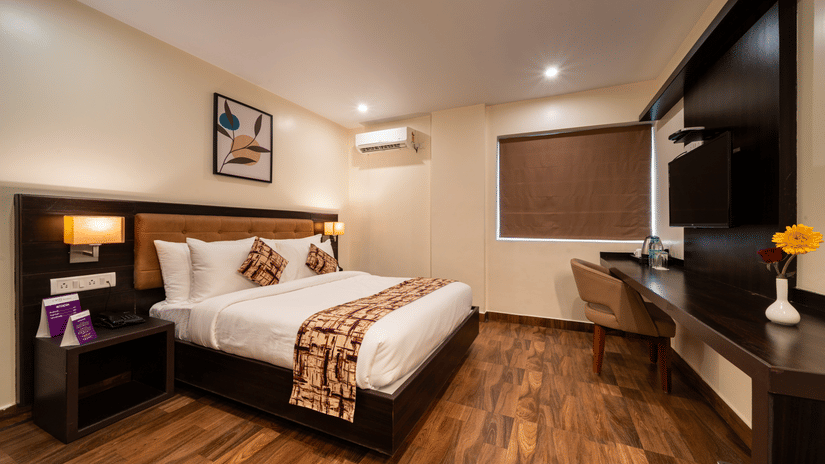 A compact, functional bedroom at VITS Select, Bengaluru, with a comfortable bed, desk, chair, and blind, ideal for accommodations in Bengaluru.
