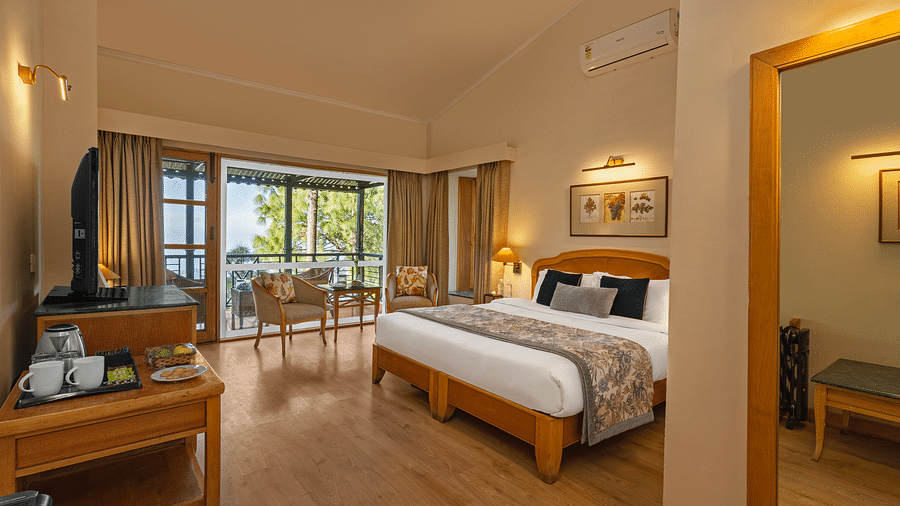 A corner view of Superior Cottage Valley view with comfy bed, table, open window and wall mirror at Baikuth resort, kasauli.