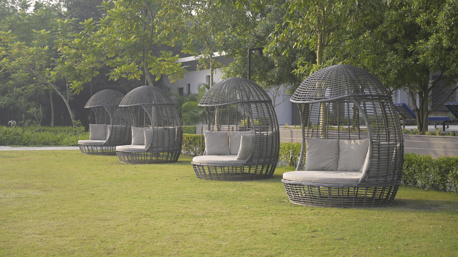 Outdoor cocoon-style seating pods arranged on a grassy lawn surrounded by trees at Hotel Sonar Bangla, Mayapur.