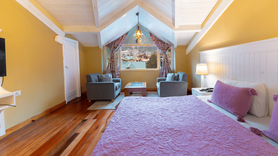 A cosy loft bedroom featuring polished wooden floors and a large window overlooking the Manali townscape - Johnson Lodge & Spa, Manali