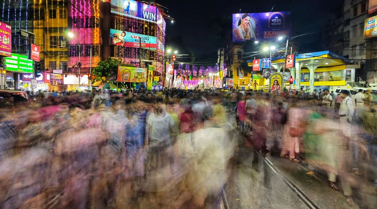 A long exposure image of a street bustling with people at night with buildings in the backdrop
