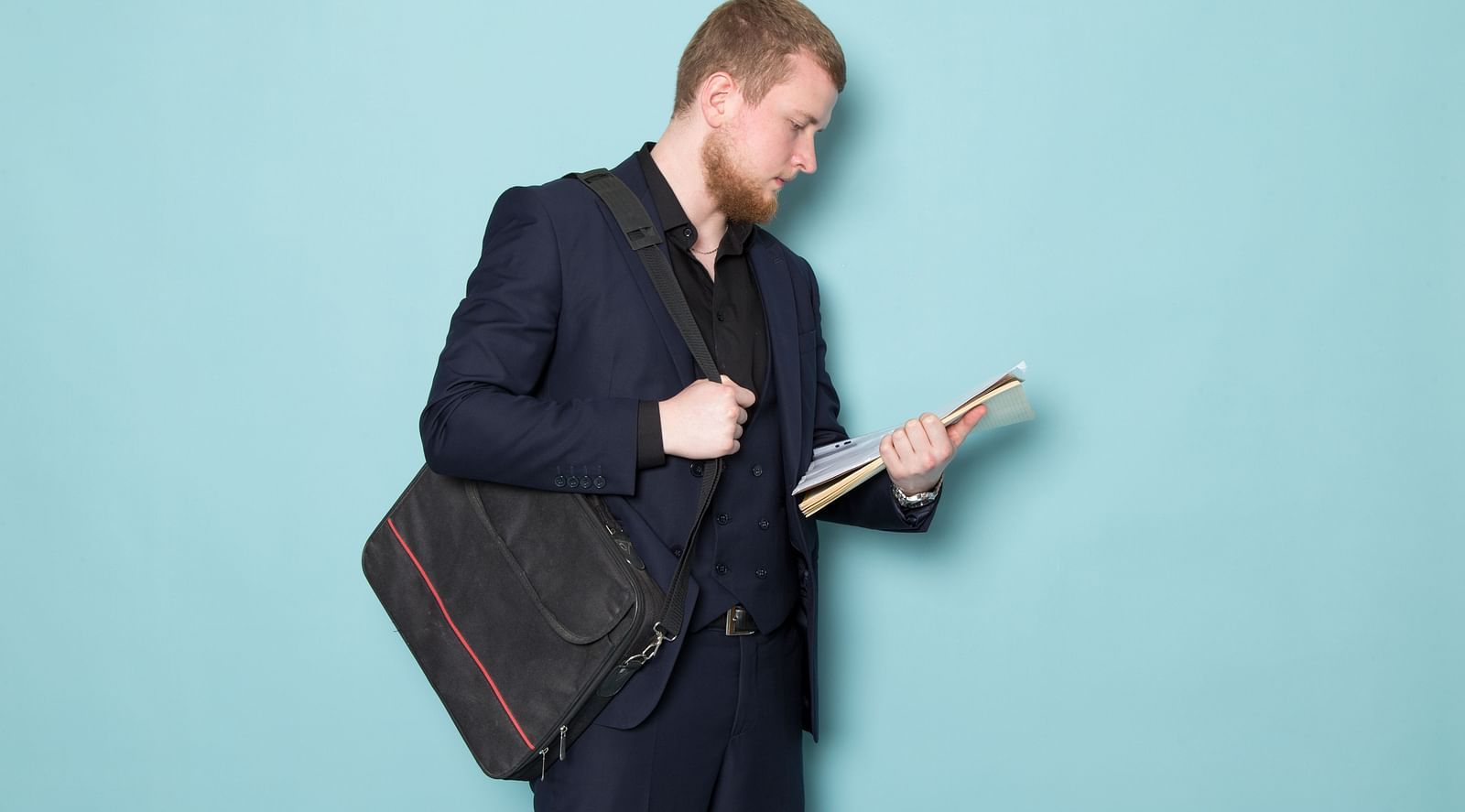 A businessman in a suit carrying a bag and holding documents in his hand.