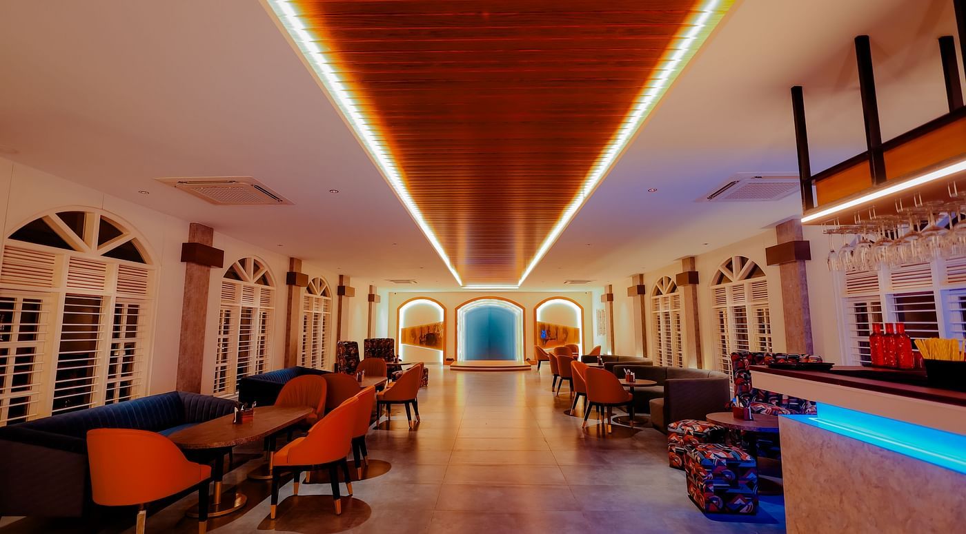 A long, brightly lit hallway with a bar area on the right, featuring colourful lighting and a modern design -  Nirantara Resort & Spa